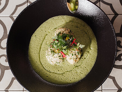 Kräuterknödel in cremiger grüner Soße mit Microgreens in schwarzer Schüssel garniert